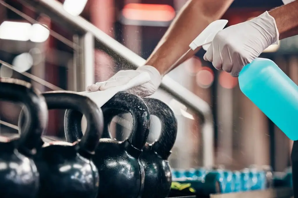 Kettlebell, cleaning service and hands cleaning at a gym with liquid soap in spray bottle with clot